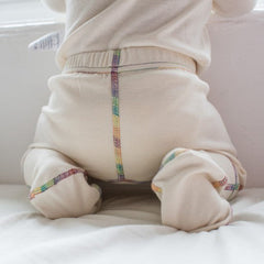 Close up of the back of the organic cotton footed pants for kids showing rainbow piping and natural white fabric.