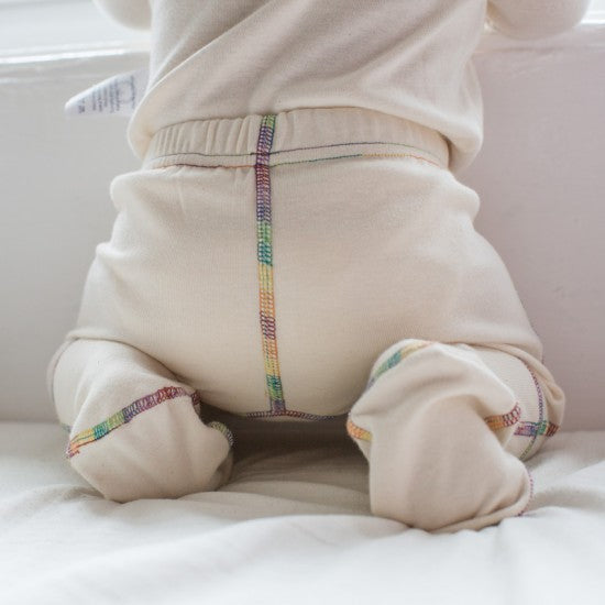 Close up of the back of the organic cotton footed pants for kids showing rainbow piping and natural white fabric.