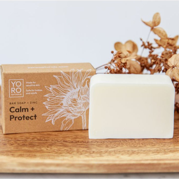 calm protect zinc cleansing bar and packaging on wood board soothes redness and irritation for eczema-prone and sensitive skin fragrance-free 2% zinc oxide